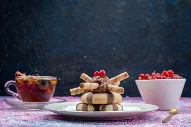 Vista frontale dei biscotti al cioccolato con mirtilli rossi e tazza di tè sulla superficie scura