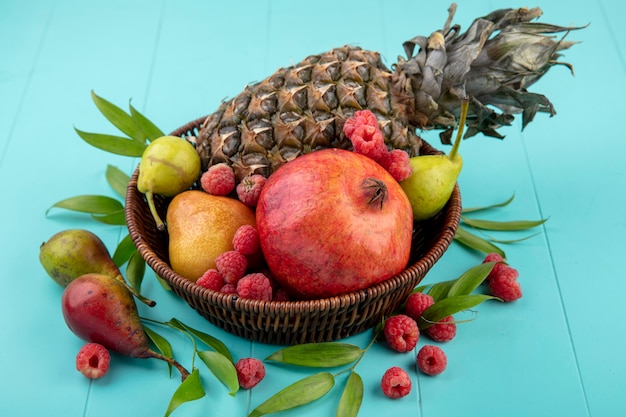 Vista frontale dei frutti come merce nel carrello del lampone della pesca del melograno dell'ananas con le foglie su superficie blu