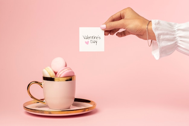 Vista frontale dei macarons in coppa d'oro per san valentino con le mani della donna