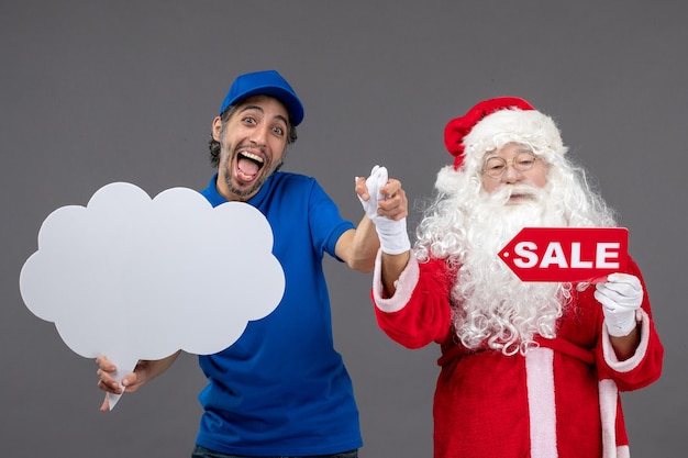 Vista frontale del babbo natale con il corriere maschio che tiene la scrittura di vendita e il segno della nuvola sul muro grigio