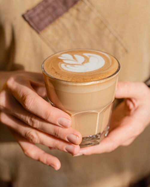 Vista frontale del barista femminile con il grembiule che tiene il bicchiere di caffè decorato