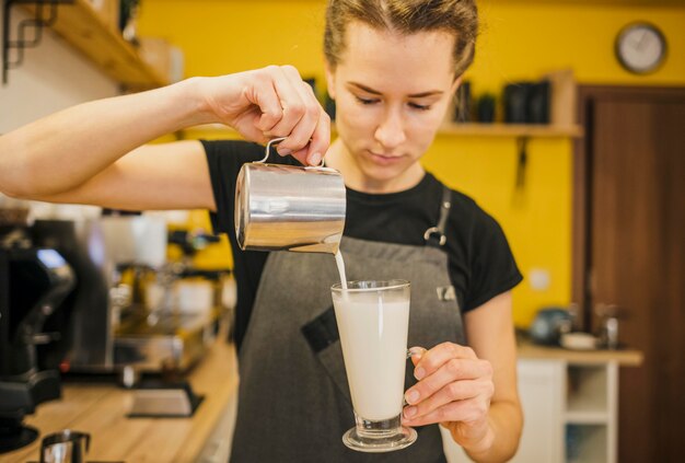 Vista frontale del barista femminile versando il latte in vetro