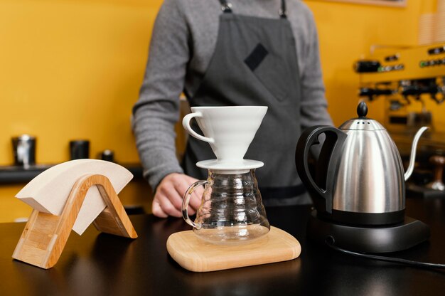 Vista frontale del barista maschio con filtro da caffè e bollitore sul bancone