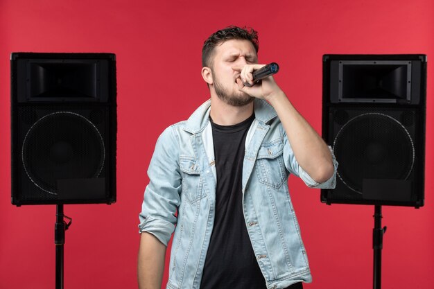 Vista frontale del cantante maschio che si esibisce sul palco con impianto stereo sulla parete rossa