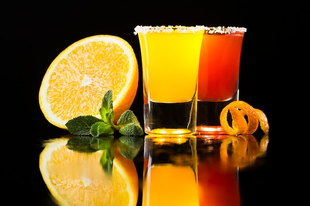 Vista frontale del cocktail rosso e giallo in bicchierini con l'arancia
