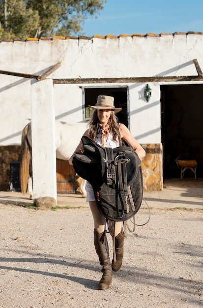 Vista frontale del coltivatore femminile che trasporta una sella di cavallo