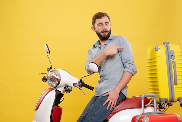 Vista frontale del concetto di viaggio con chiedendosi giovane uomo seduto sulla moto con le valigie che punta indietro su di esso su giallo