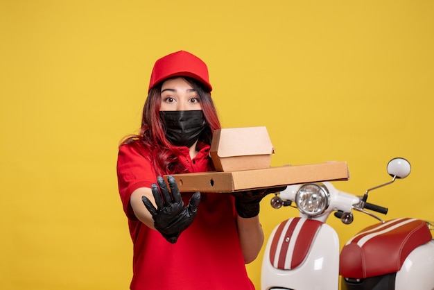 Vista frontale del corriere femminile in maschera con cibo di consegna sulla parete gialla