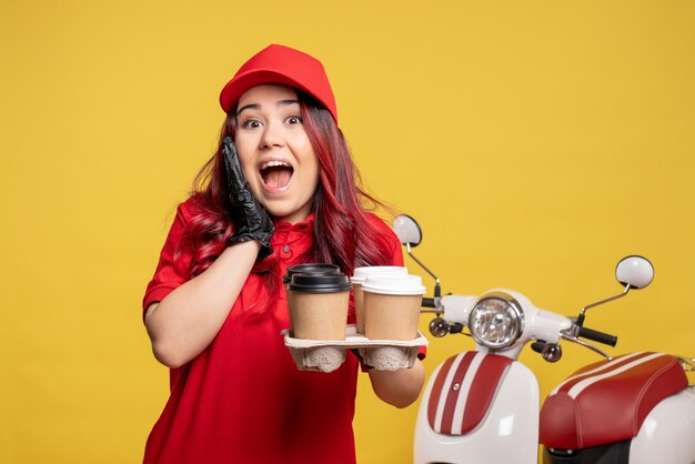 Vista frontale del corriere femminile in uniforme rossa con caffè sulla parete gialla