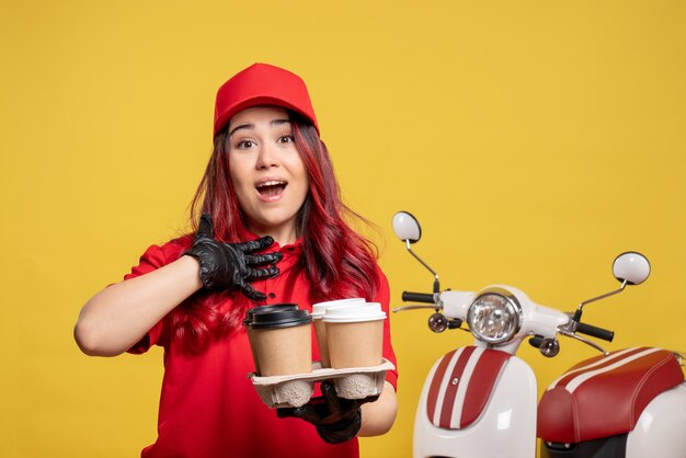 Vista frontale del corriere femminile in uniforme rossa con caffè sulla parete gialla