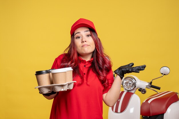 Vista frontale del corriere femminile in uniforme rossa con caffè sulla parete gialla