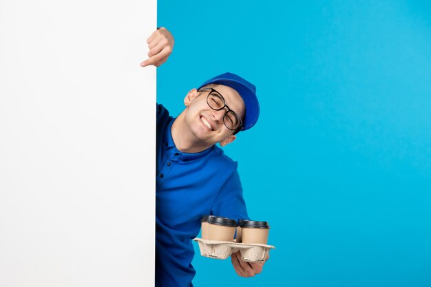 Vista frontale del corriere maschio in uniforme blu con caffè sull'azzurro