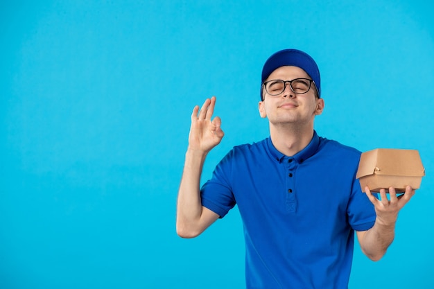 Vista frontale del corriere maschio in uniforme blu con poca confezione di cibo sull'azzurro