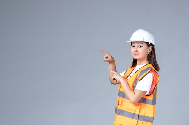 Vista frontale del costruttore femminile in uniforme che sorride sul muro bianco