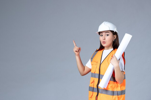 Vista frontale del costruttore femminile in uniforme con poster in mano sul muro grigio