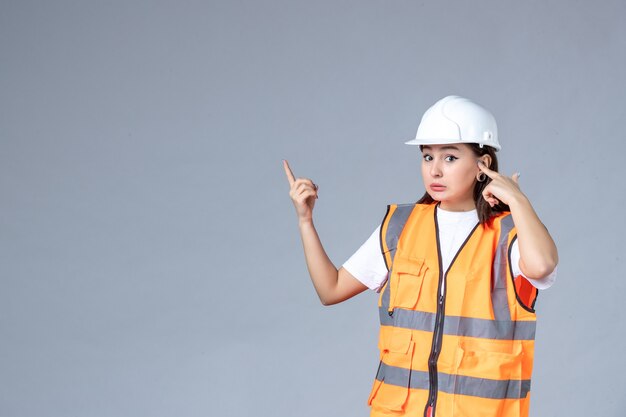 Vista frontale del costruttore femminile in uniforme sul muro bianco