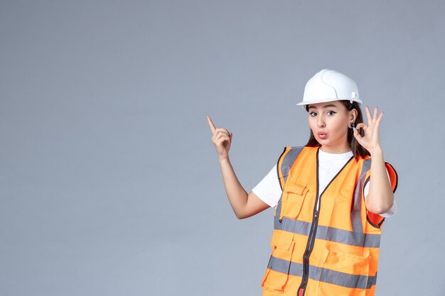 Vista frontale del costruttore femminile in uniforme sul muro bianco