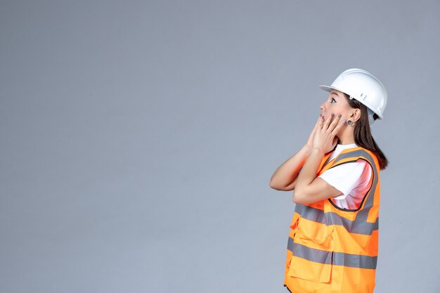 Vista frontale del costruttore femminile in uniforme sul muro bianco