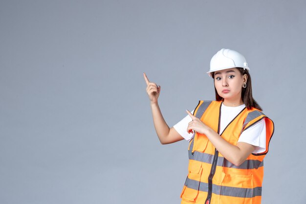 Vista frontale del costruttore femminile in uniforme sul muro grigio