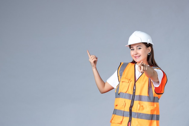 Vista frontale del costruttore femminile in uniforme sul muro grigio