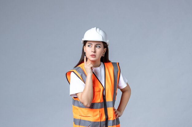 Vista frontale del costruttore femminile in uniforme sul muro grigio