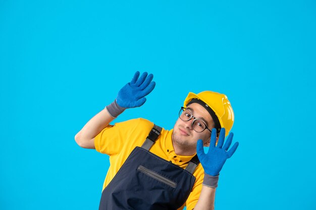 Vista frontale del costruttore maschio in uniforme e casco con i guanti sulla superficie blu