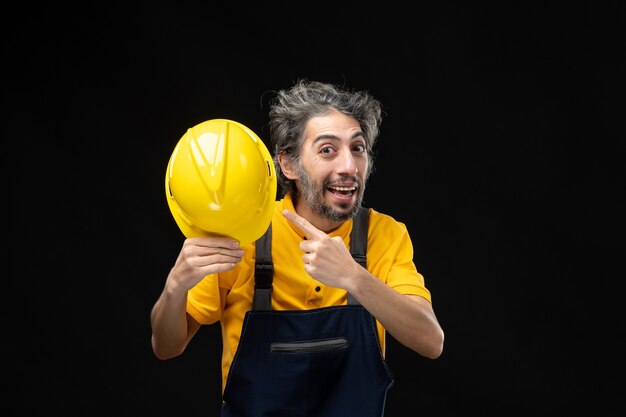 Vista frontale del costruttore maschio in uniforme gialla sul muro nero