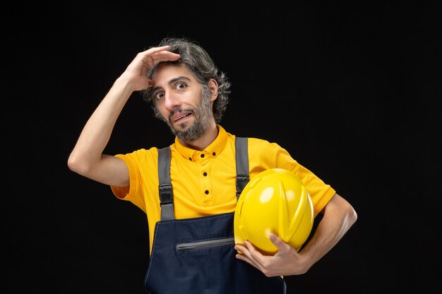 Vista frontale del costruttore maschio in uniforme gialla sul muro nero