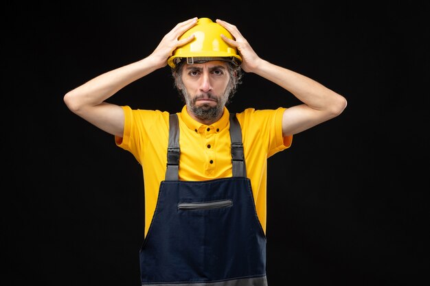 Vista frontale del costruttore maschio in uniforme gialla sul muro nero