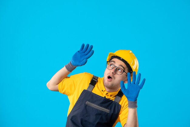 Vista frontale del costruttore maschio spaventato in uniforme e guanti su un blu