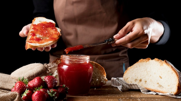 Vista frontale del cuoco unico che spande l'ostruzione di fragola su pane