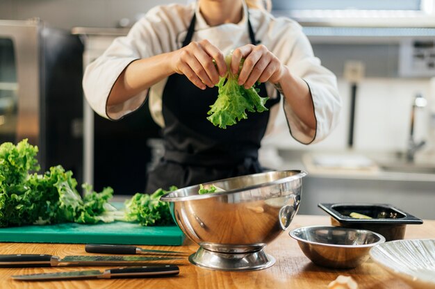 Vista frontale del cuoco unico femminile che strappa insalata in cucina