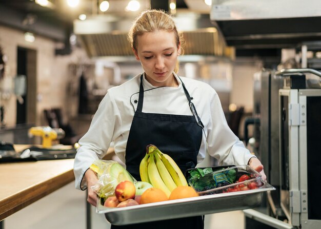 Vista frontale del cuoco unico femminile che tiene vassoio con frutta