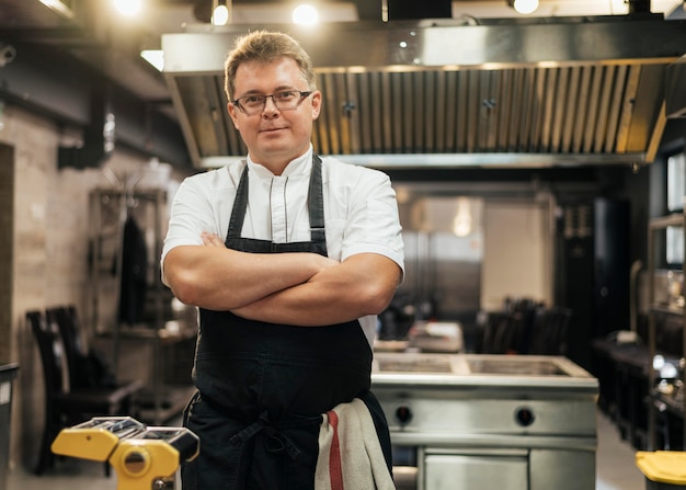 Vista frontale del cuoco unico maschio in posa con le braccia incrociate in cucina