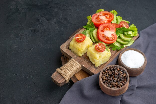 Vista frontale del formaggio di verdure fresche tritate sul tagliere e spezie su asciugamano di colore scuro su superficie nera