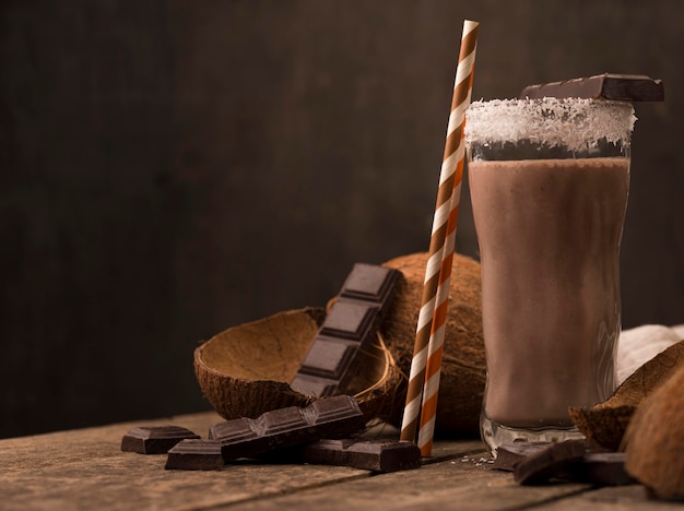 Vista frontale del frullato di vetro sul vassoio con cocco e cioccolato