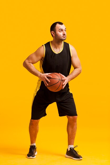 Vista frontale del giocatore di pallacanestro maschio che posa con la palla