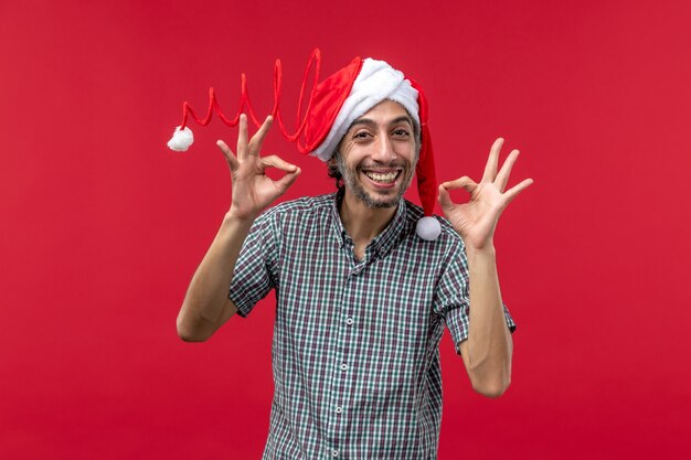 Vista frontale del giovane che indossa il cappello di Natale giocattolo sulla parete rossa