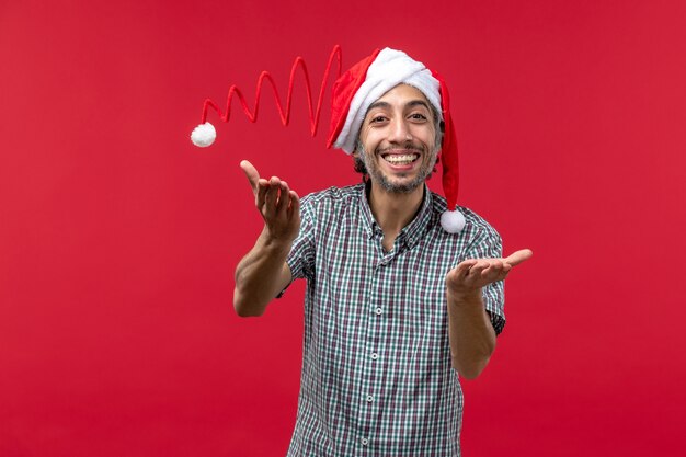 Vista frontale del giovane che indossa il cappello di Natale giocattolo sulla parete rossa