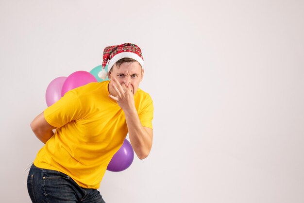 Vista frontale del giovane che nasconde palloncini colorati dietro la schiena sul muro bianco