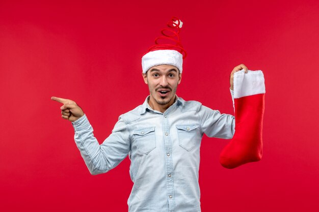 Vista frontale del giovane che propone con il calzino di Natale sulla parete rossa