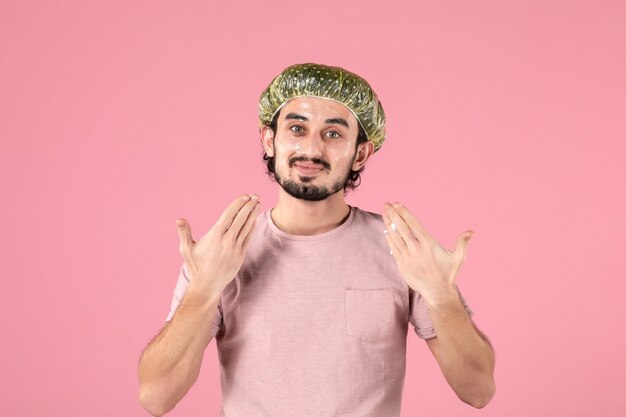 vista frontale del giovane che si applica la maschera sul viso sul muro rosa