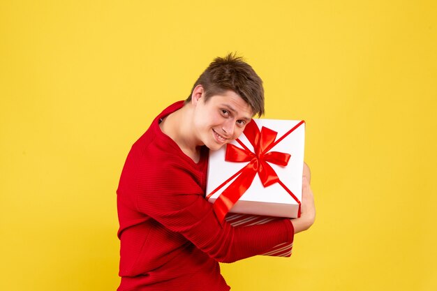 Vista frontale del giovane che tiene grande regalo di Natale sulla parete gialla