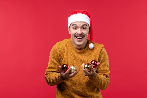 Vista frontale del giovane che tiene i giocattoli dell'albero di Natale sulla parete rossa