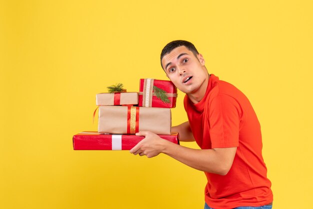 Vista frontale del giovane che tiene i regali di Natale sulla parete gialla