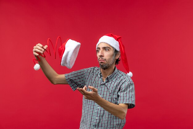 Vista frontale del giovane che tiene il cappuccio del giocattolo di Natale sulla parete rossa