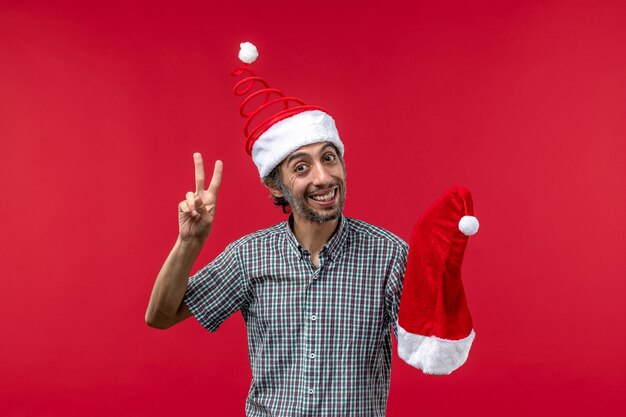 Vista frontale del giovane che tiene il cappuccio di Natale sulla parete rossa