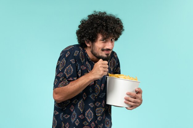 Vista frontale del giovane che tiene il cestino con le patatine fritte e guardare film sul cinema maschio del cinema del film della parete blu