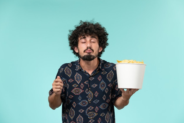 Vista frontale del giovane che tiene il cestino con le patatine fritte e guardare film sul maschio del cinema di film del cinema della parete blu