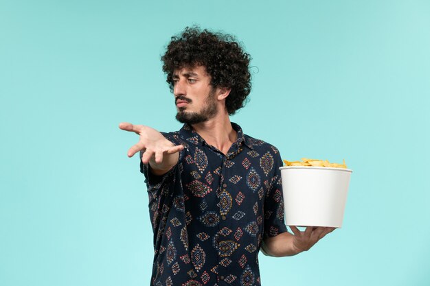 Vista frontale del giovane che tiene il cestino con le patatine fritte e guardare il film sul cinema maschio di film del cinema della parete blu